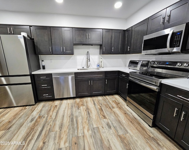 kitchen featuring appliances with stainless steel finishes, light hardwood / wood-style floors, sink, and decorative backsplash