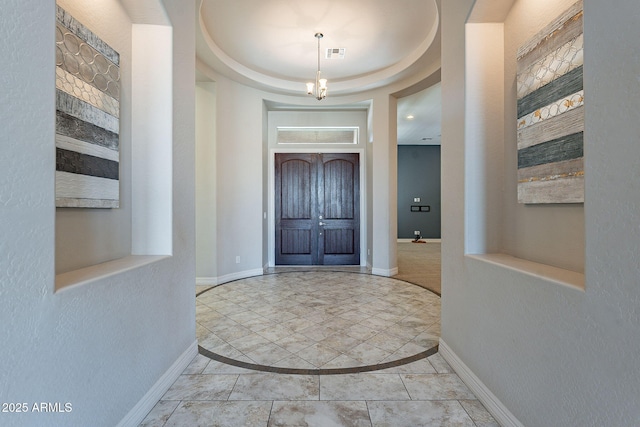 entryway featuring visible vents, an inviting chandelier, a raised ceiling, and baseboards