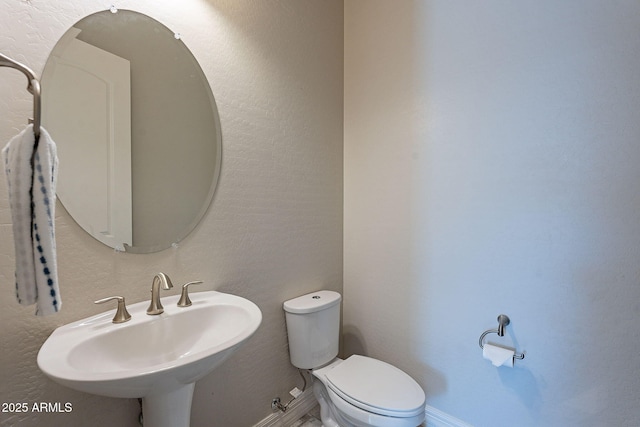 bathroom featuring toilet, a textured wall, baseboards, and a sink