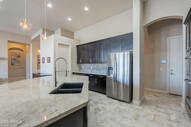 kitchen featuring pendant lighting, a sink, light stone counters, stainless steel fridge, and decorative backsplash