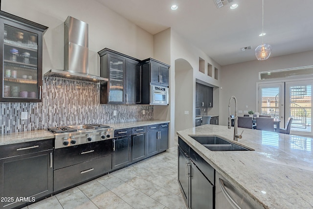 kitchen with light stone counters, visible vents, stainless steel appliances, a sink, and wall chimney range hood