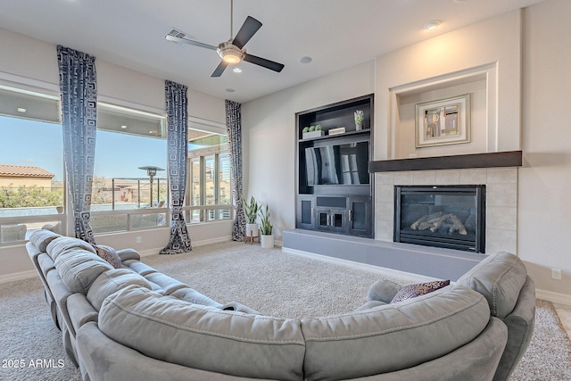 carpeted living room with a tiled fireplace, built in shelves, a ceiling fan, and baseboards