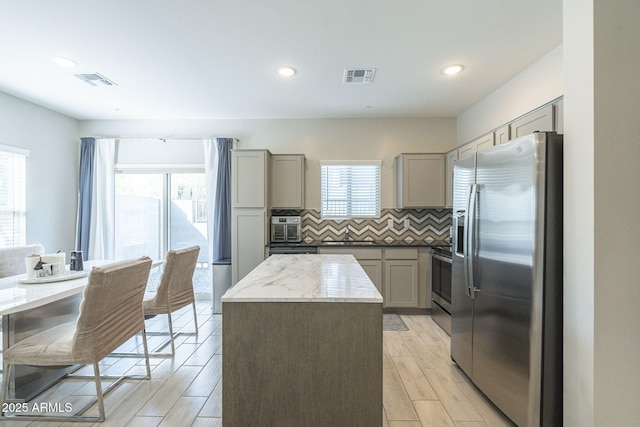 kitchen featuring light stone countertops, tasteful backsplash, stainless steel appliances, a center island, and gray cabinets