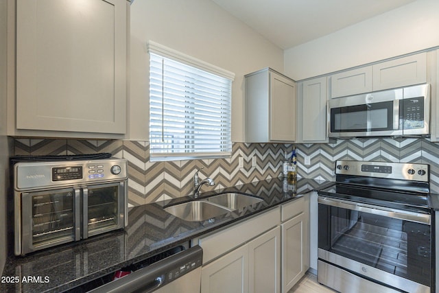 kitchen featuring backsplash, stainless steel appliances, sink, dark stone countertops, and gray cabinets