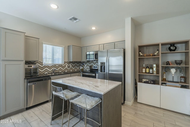 kitchen featuring appliances with stainless steel finishes, light stone counters, gray cabinetry, sink, and a center island