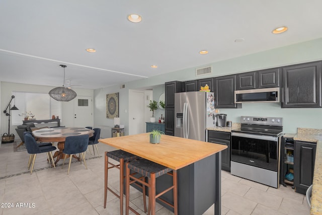 kitchen with light stone countertops, pendant lighting, light tile patterned floors, appliances with stainless steel finishes, and a kitchen bar