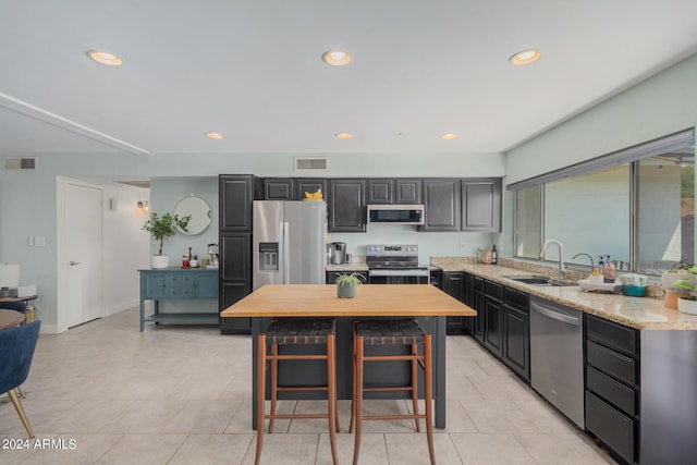 kitchen featuring light stone countertops, appliances with stainless steel finishes, a center island, a breakfast bar, and sink