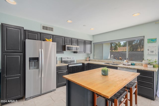 kitchen with light tile patterned flooring, stainless steel appliances, sink, and a kitchen island