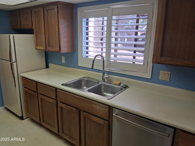 kitchen featuring light floors, freestanding refrigerator, light countertops, dishwasher, and a sink