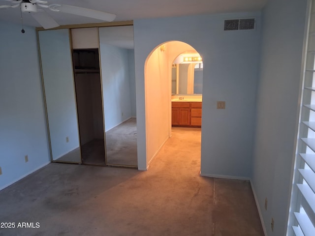 unfurnished bedroom with a closet, visible vents, light carpet, baseboards, and arched walkways
