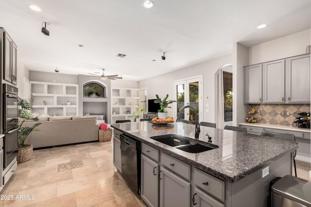 kitchen featuring black dishwasher, a center island with sink, arched walkways, open floor plan, and a sink