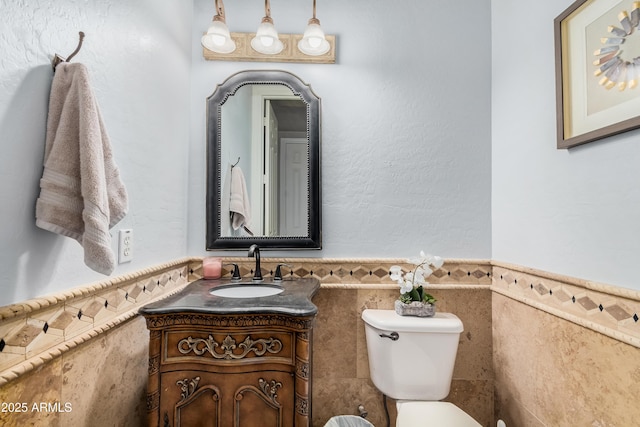 half bath with toilet, vanity, tile walls, and wainscoting