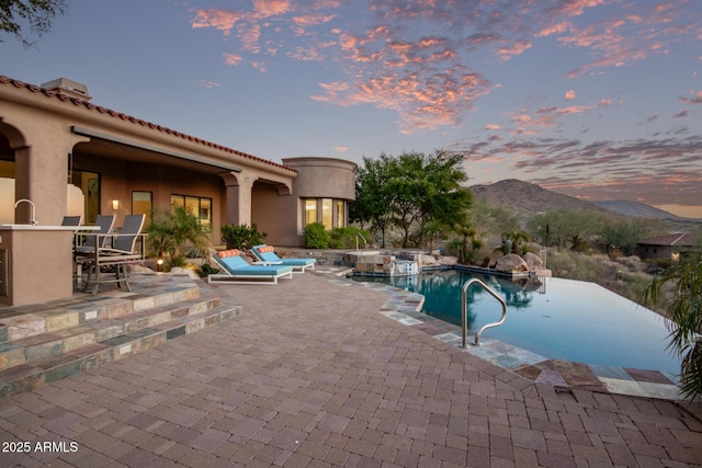 pool at dusk featuring pool water feature, a mountain view, and a patio area