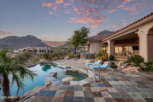 pool at dusk featuring an in ground hot tub, a mountain view, and a patio