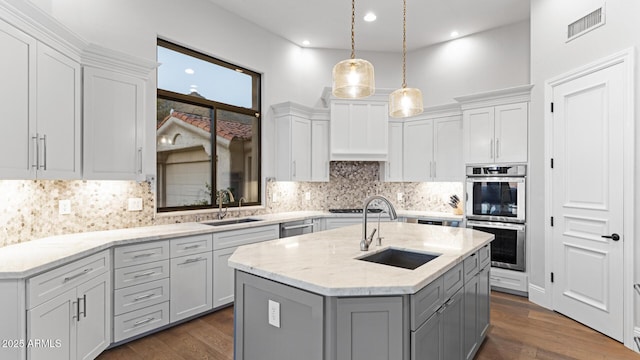 kitchen with appliances with stainless steel finishes, sink, a center island with sink, and decorative light fixtures