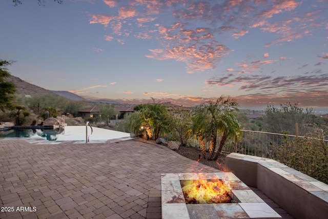 patio terrace at dusk featuring a mountain view, a fenced in pool, and an outdoor fire pit