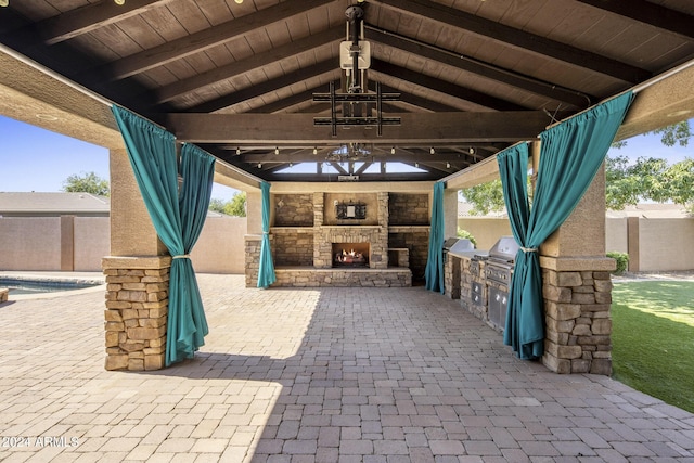 view of patio featuring ceiling fan, an outdoor kitchen, and an outdoor stone fireplace