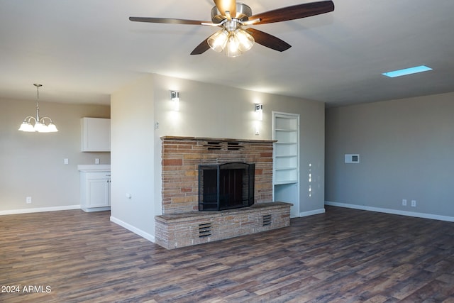 unfurnished living room featuring ceiling fan with notable chandelier, dark wood-type flooring, a fireplace, and built in shelves