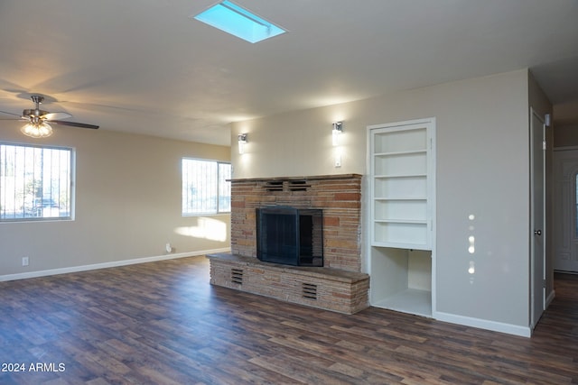 unfurnished living room featuring dark wood-type flooring, a stone fireplace, built in shelves, and ceiling fan