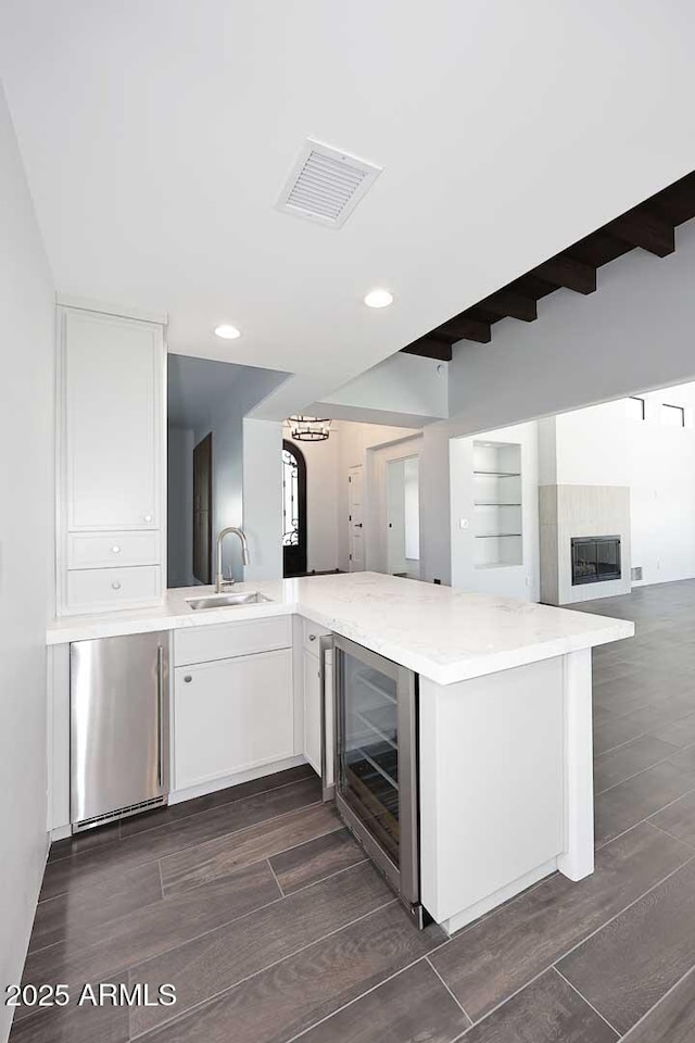 kitchen with white cabinetry, wine cooler, sink, kitchen peninsula, and stainless steel refrigerator