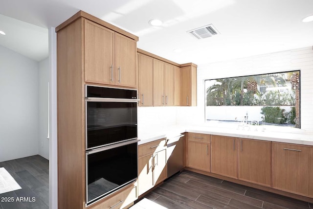 kitchen with black double oven, light brown cabinetry, and light stone counters