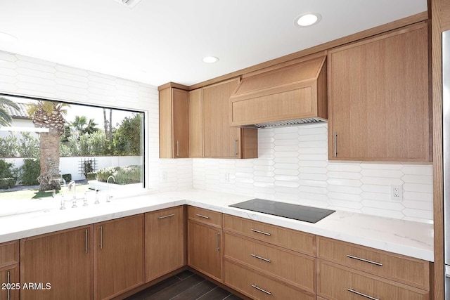 kitchen featuring light stone countertops, custom exhaust hood, dark wood-type flooring, black electric stovetop, and decorative backsplash