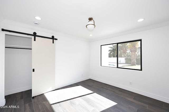 unfurnished bedroom with a closet, crown molding, and a barn door