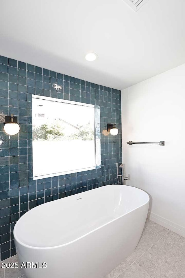 bathroom with a washtub, tile patterned flooring, and tile walls