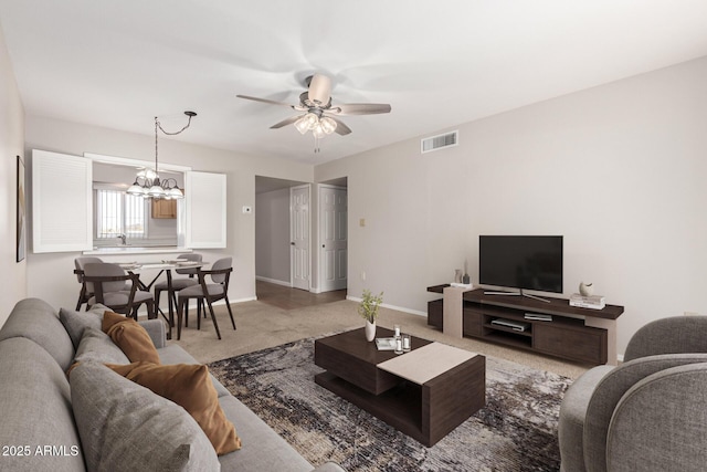 carpeted living room with ceiling fan with notable chandelier