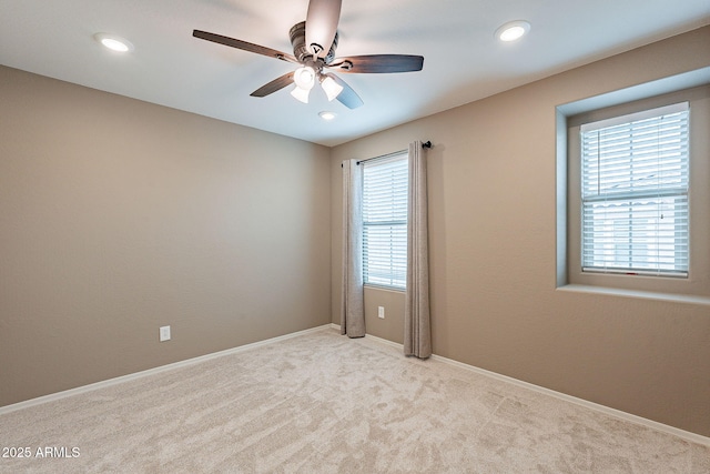 unfurnished room with a wealth of natural light, baseboards, light colored carpet, and ceiling fan