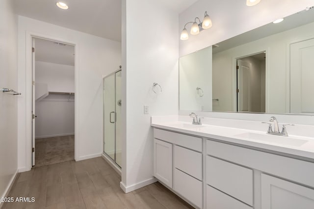 full bath featuring a sink, a walk in closet, a stall shower, and wood finished floors