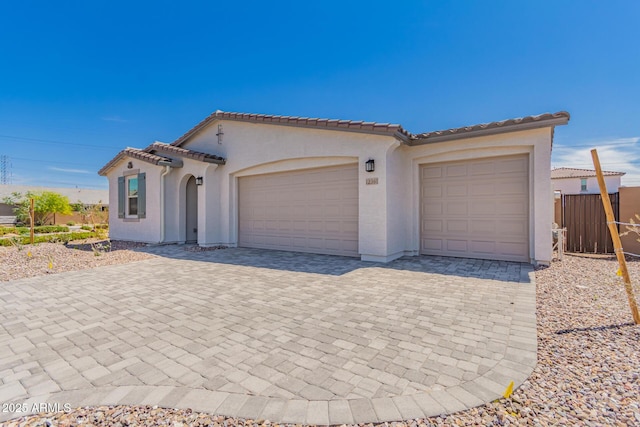 mediterranean / spanish-style house with a tiled roof, a garage, fence, stucco siding, and decorative driveway