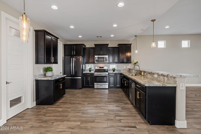 kitchen with hanging light fixtures, kitchen peninsula, stainless steel appliances, light hardwood / wood-style flooring, and sink