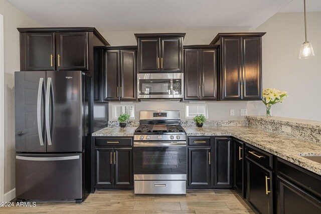 kitchen with pendant lighting, light wood-type flooring, light stone counters, appliances with stainless steel finishes, and dark brown cabinetry