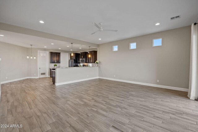 unfurnished living room featuring ceiling fan with notable chandelier and light wood-type flooring