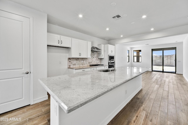 kitchen featuring a large island, gas stovetop, light stone countertops, light hardwood / wood-style floors, and white cabinets