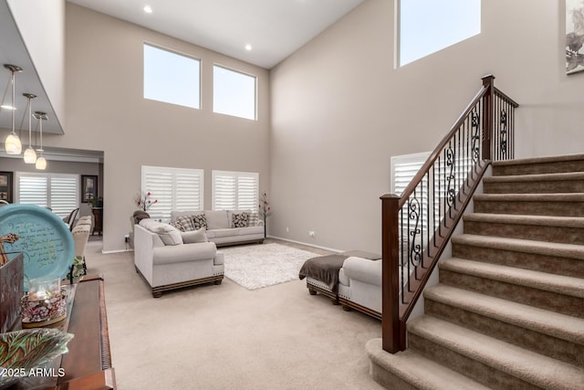 living area featuring a healthy amount of sunlight, light colored carpet, stairway, and baseboards