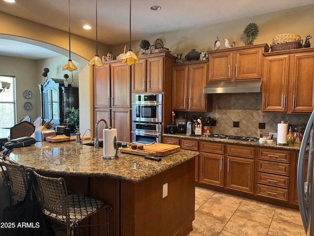 18008 W Ocotillo Ave, Goodyear, AZ 85338 - kitchen with arched walkways, double oven, under cabinet range hood, brown cabinetry, and tasteful backsplash