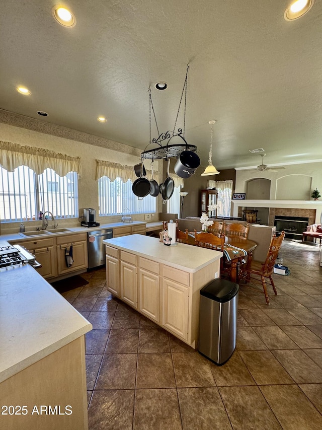 kitchen featuring light countertops, a tiled fireplace, light brown cabinets, a sink, and dishwasher