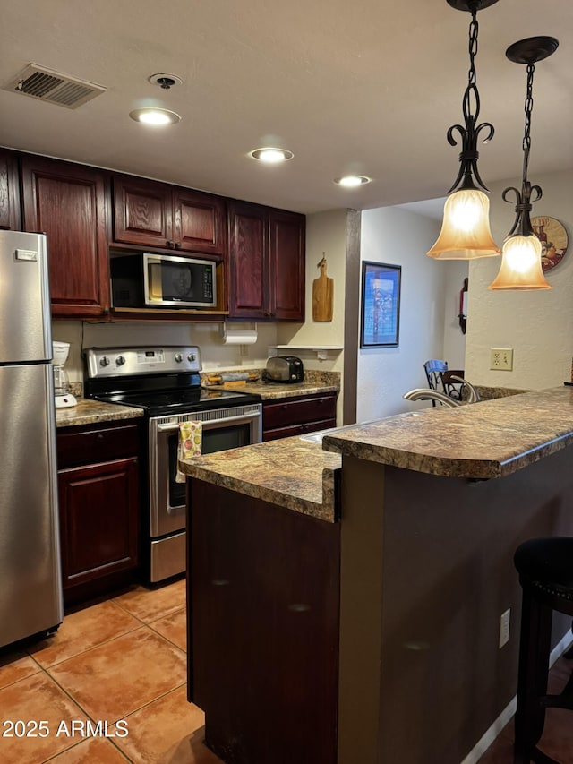 12123 W Bell Rd Unit 337, Surprise, AZ 85378 - kitchen with appliances with stainless steel finishes, a kitchen bar, a peninsula, hanging light fixtures, and light tile patterned floors