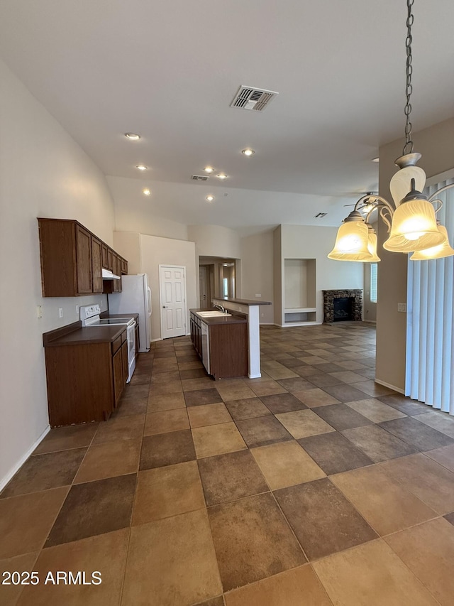 kitchen featuring a stone fireplace, white appliances, a sink, visible vents, and open floor plan