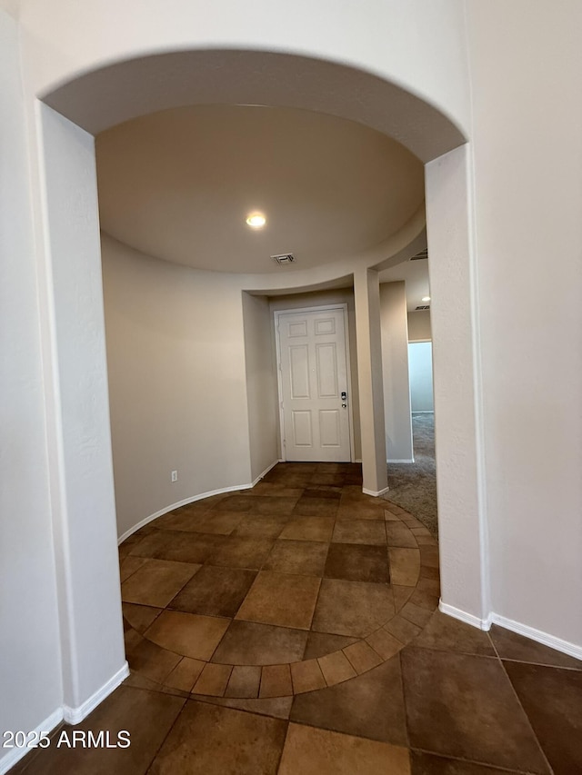 hallway featuring arched walkways, visible vents, and baseboards