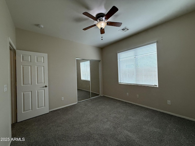 unfurnished bedroom featuring ceiling fan, visible vents, baseboards, a closet, and dark colored carpet