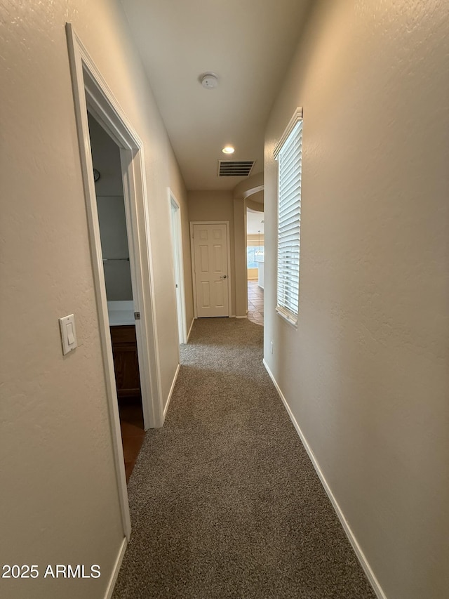 hall with carpet, visible vents, and baseboards