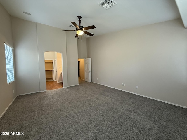 unfurnished bedroom featuring arched walkways, high vaulted ceiling, visible vents, baseboards, and dark carpet