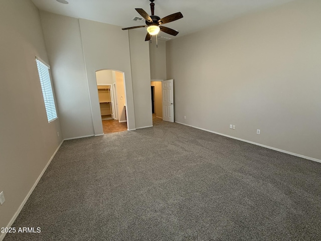 unfurnished bedroom featuring arched walkways, a walk in closet, dark carpet, high vaulted ceiling, and baseboards