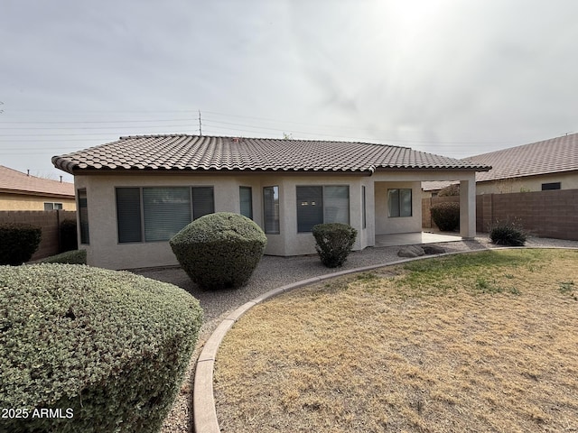 rear view of house with a tile roof, fence, a lawn, stucco siding, and a patio area