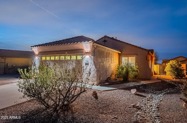 view of front of home featuring a garage, a tile roof, fence, and stucco siding