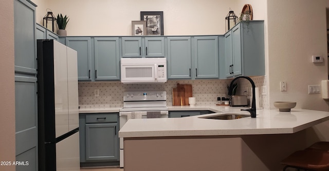 2004 N 108th Dr, Avondale, AZ 85392 - kitchen with white appliances, a peninsula, backsplash, a kitchen bar, and light countertops
