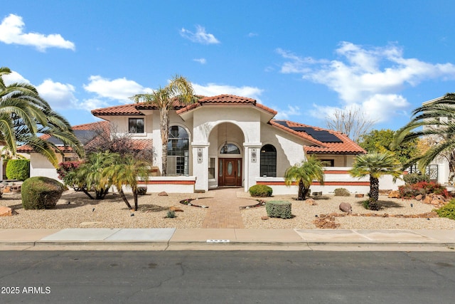 mediterranean / spanish-style house with stucco siding, a tiled roof, and solar panels